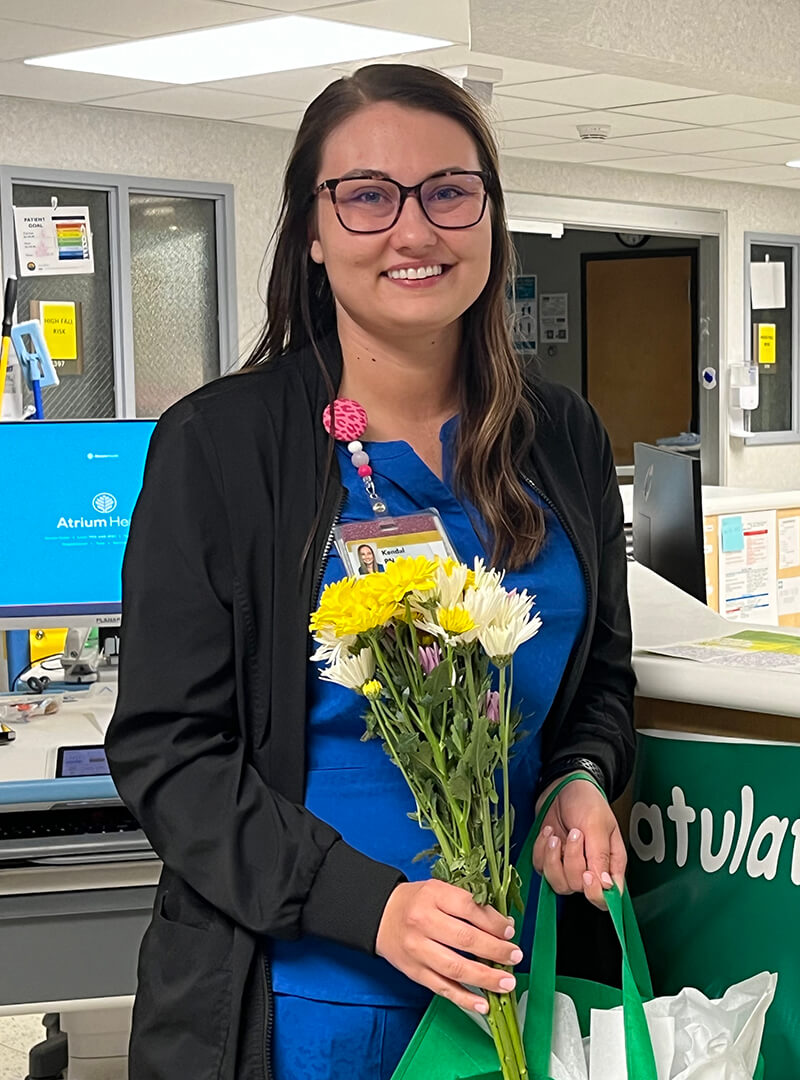 Kendal Stuart, wearing medical scrubs holding yellow flowers while smiling.